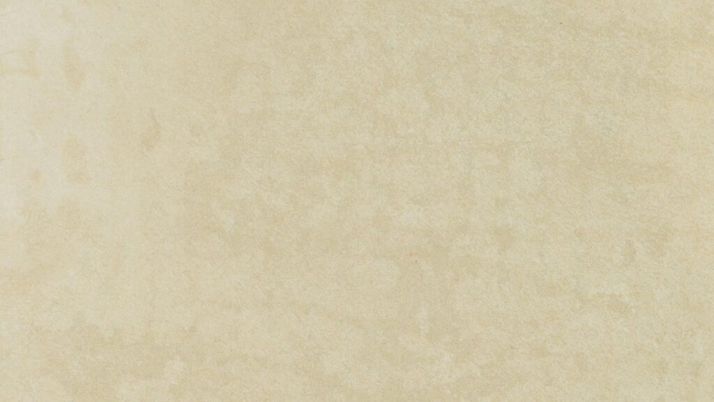 A close-up of a textured, light beige surface. The material has a slightly mottled appearance, giving it a subtle pattern with various shades of beige and cream.