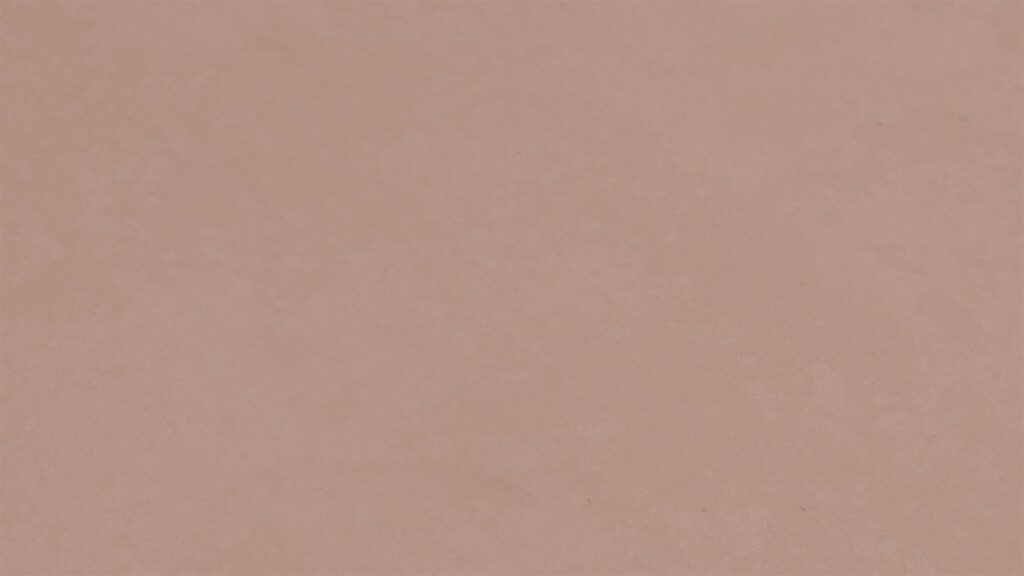 A close-up view of a light peach-colored surface with a slightly mottled texture. The surface is flat and uniformly colored, with subtle variations in shade creating a soft, abstract pattern.