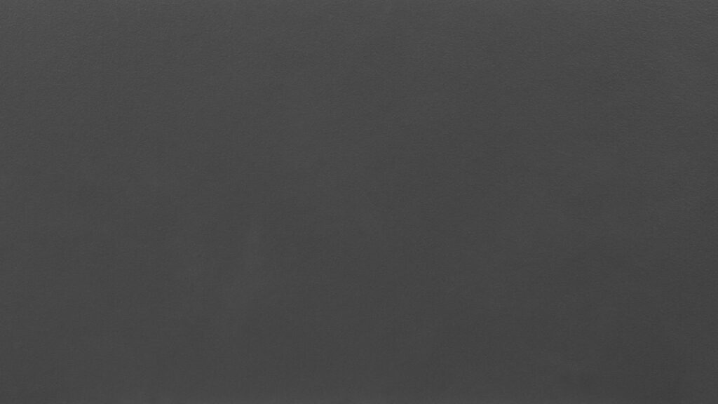 A close-up of a dark gray, textured surface. The material appears smooth and slightly matte with a uniform color throughout. There are no visible patterns, markings, or objects, just an expanse of the dark gray texture.